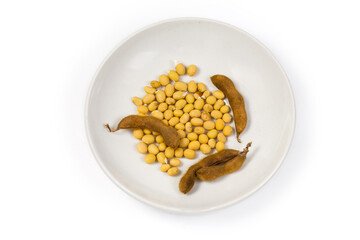 Top view of soybean seeds and pods on white saucer