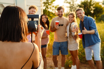 Multiracial friends drinking beverages and taking instant photo by trailer
