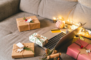  Online shopping at Christmas holidays. Gifts, and mock up screen laptop on couch with natural eco presents and decor. Merry Christmas. Wrapping present boxes