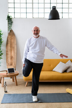 Active Senior Man Stretching Legs On Exercise Mat At Home