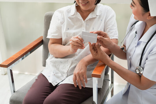 Female Nurse And Senior Woman At Hospital With Health Insurance Card