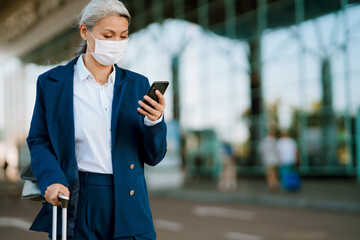 Grey asian woman in face mask using cellphone on airport parking
