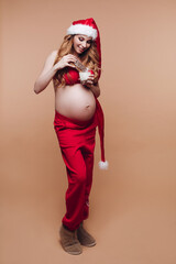Young beautiful pregnant woman in a Santa costume eats Tula gingerbread with a cup of milk