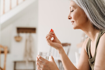 Mature asian woman taking her medication while sitting on couch