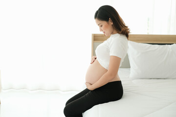 portrait asia young pregnant woman sit on the bed with hand on belly