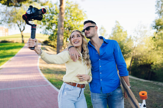 Smiling girlfriend vlogging with boyfriend through camera on footpath