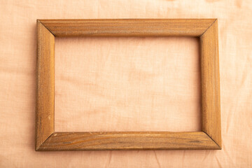 Wooden frame on smooth orange linen tissue. Top view, natural textile background.