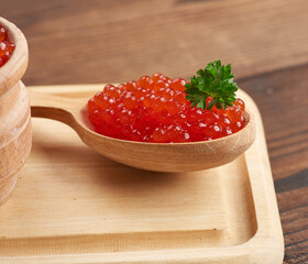 red caviar of pink salmon lies in a wooden spoon on a brown wooden table