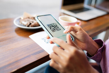 Woman scanning QR code through mobile phone at cafe table