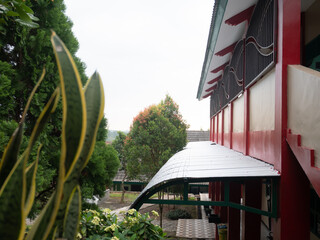 Peaceful view of a building's exterior with a covered walkway and red trim, featuring lush garden...