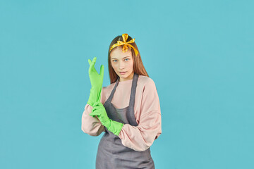 Ready For Spring-Cleaning. Portrait of joyful girl with household supplies in hands over blue background. Younng woman with rubber protective gloves.