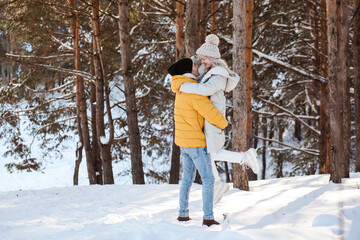 Fototapeta na wymiar Good-looking couple is having fun in winter forest, spending Christmas holidays outdoors.