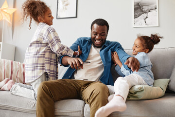 Portrait of two African-American girls playing with father in cozy home interior