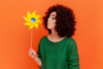 Side view of childish woman with Afro hairstyle wearing green casual style sweater playing blowing...