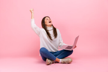 Extremely happy female sitting on floor with laptop yelling, celebrating her victory or success,...