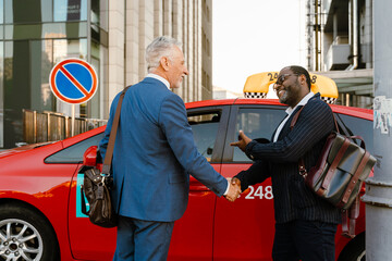 Multiracial men smiling and handshaking while standing by taxi