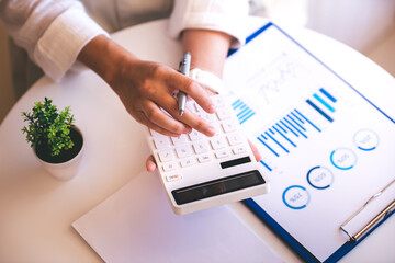 A young woman's hand presses a calculator to determine and summarize the cost of mortgage home loans for refinancing plans, lifestyle concepts.