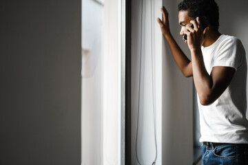 Fototapeta na wymiar Young black man talking on cellphone while looking at window