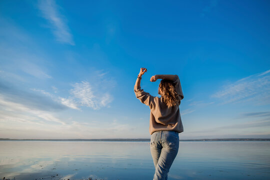 Woman with arms raised standing at lake