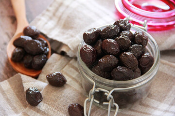 Black olives in glassware and wooden spoon
