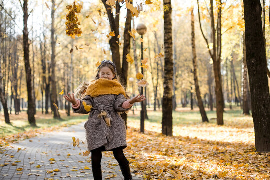 Carefree girl throwing autumn leaves on walkway in park