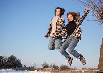 cheerful happy teenagers guy and girl in plaid shirts and jeans bouncing up outdoors against blue sky. freedom, carelessness, lifestyle, emotions of joy. Valentine's Day. Selective focus