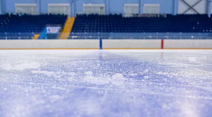 Clean empty ice hockey rink. Skate blade marks and snow crumbs. Empty stands in background.