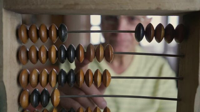 Senior accountant wearing glasses calculating home budget with antique wooden abacus. Housekeeping and financial concept.