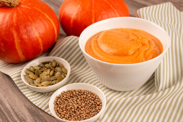 Hokkaido pumpkin cream soup in a white bowl on wooden table background. Vegan food concept, homemade soup recipe. Selective focus