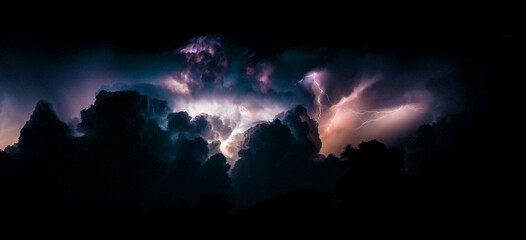 Flashes of lightning and clouds during thunderstorms at night. Panoramic photo.