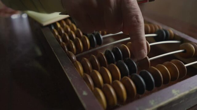 Mature man counting with vintage wooden abacus and writing data to paper notepad by pencil. Home finance concept.