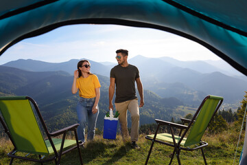 Couple and cool box with bottles of beer in mountains, view from tent