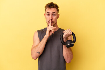 Young sport man holding a dumbbell isolated on yellow background keeping a secret or asking for silence.