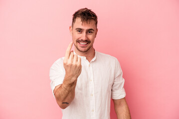 Young caucasian man isolated on pink background pointing with finger at you as if inviting come closer.