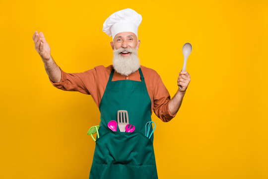 Portrait of attractive cheery grey-haired man chef holding spoon domestic culinary hobby isolated over bright yellow color background