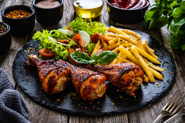 Barbecue chicken drumsticks with chips and greens  on wooden table
