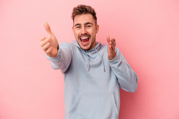 Young caucasian man isolated on pink background feels confident giving a hug to the camera.