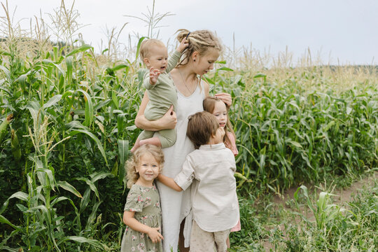 Siblings embracing mother standing with toddler girl in corn field