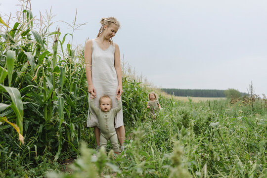 Woman assisting toddler girl to walk in corn field