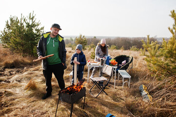 Family barbecuing on a deck in the pine forest. Bbq day with grill.