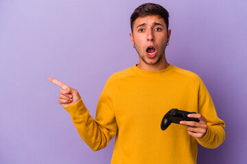 Young caucasian man holding game controller isolated on purple background  pointing to the side