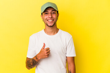 Young caucasian man with tattoos isolated on yellow background  smiling and raising thumb up