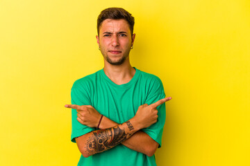 Young caucasian man with tattoos isolated on yellow background  points sideways, is trying to...