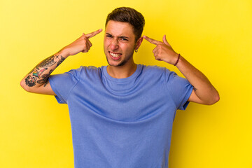 Young caucasian man with tattoos isolated on yellow background  showing a disappointment gesture with forefinger.