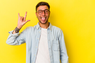 Young caucasian man with tattoos isolated on yellow background  showing rock gesture with fingers