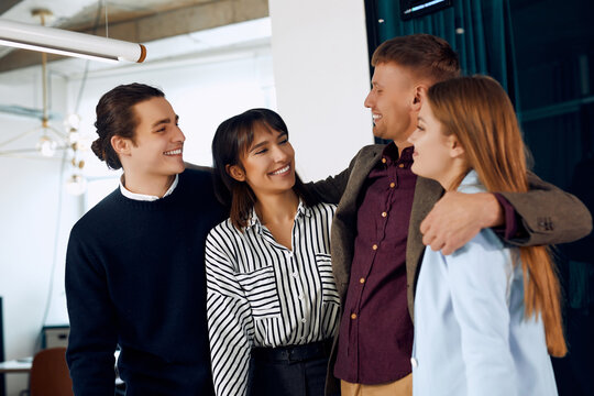 A group of happy office workers are hugging and smiling at each other.