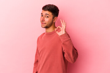 Young caucasian man with tattoos isolated on yellow background  winks an eye and holds an okay gesture with hand.