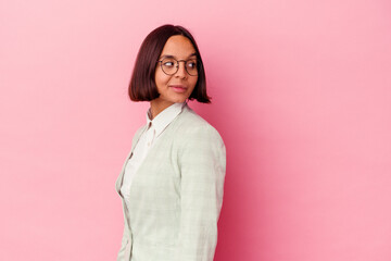 Fototapeta premium Young mixed race woman wearing a green suit isolated on pink background looks aside smiling, cheerful and pleasant.