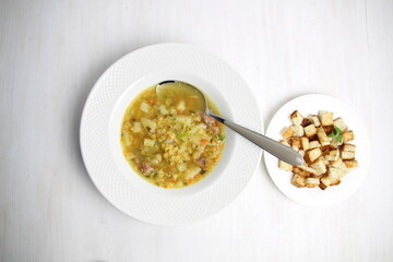 Pea soup with potato and meat in white plate with spoon and toast