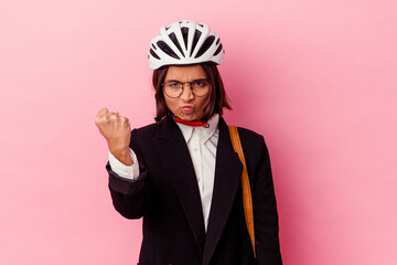 Young business mixed race woman wearing a bike helmet isolated on pink background showing fist to camera, aggressive facial expression.